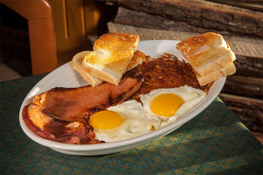 Platter with two sunny-side-up eggs, ham steak, hash browns and toast
