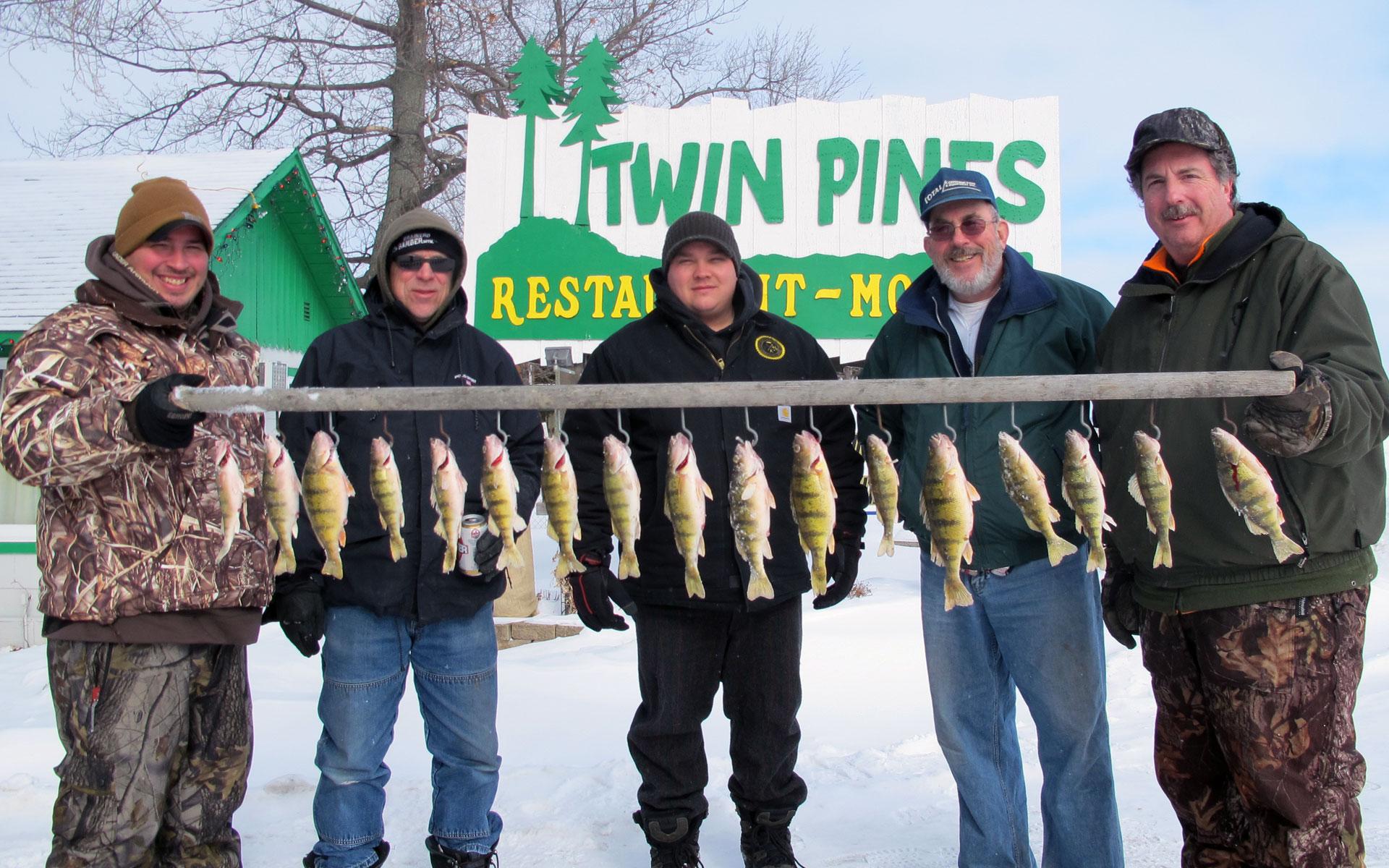 5 fishermen holding strung row of perch fish in winter